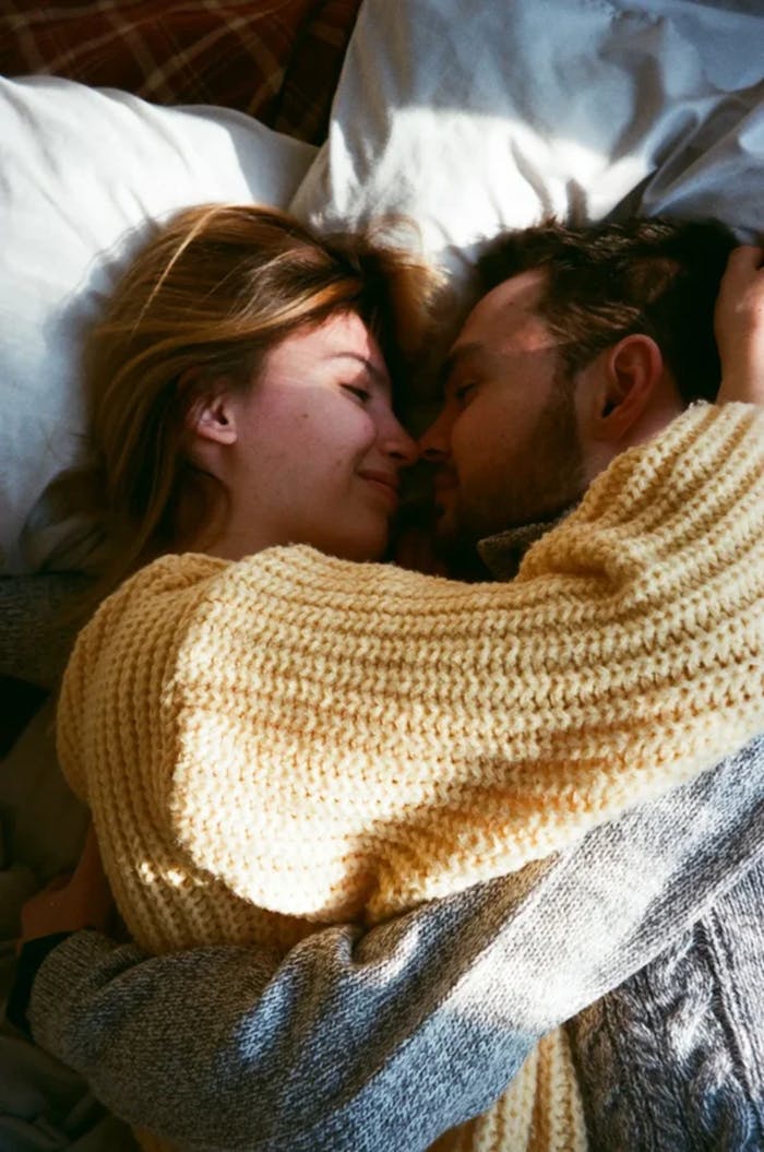 A loving couple embraces warmly on a bed, wrapped in sweaters, filled with affection.